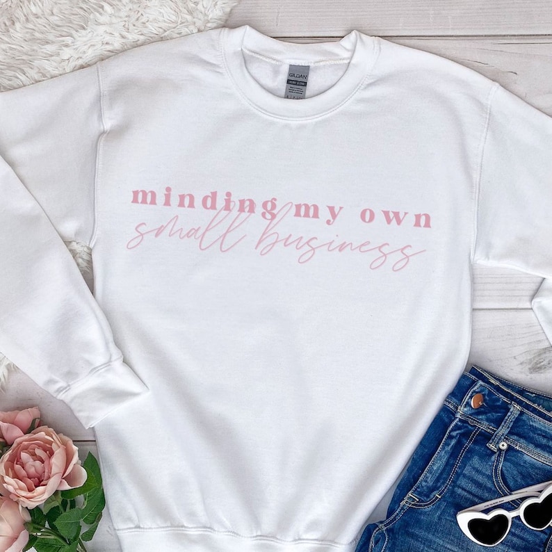 K&ouml;nnte beinhalten: Wei&szlig;er Pullover mit dem Text "minding my own small business" in rosa Schrift.