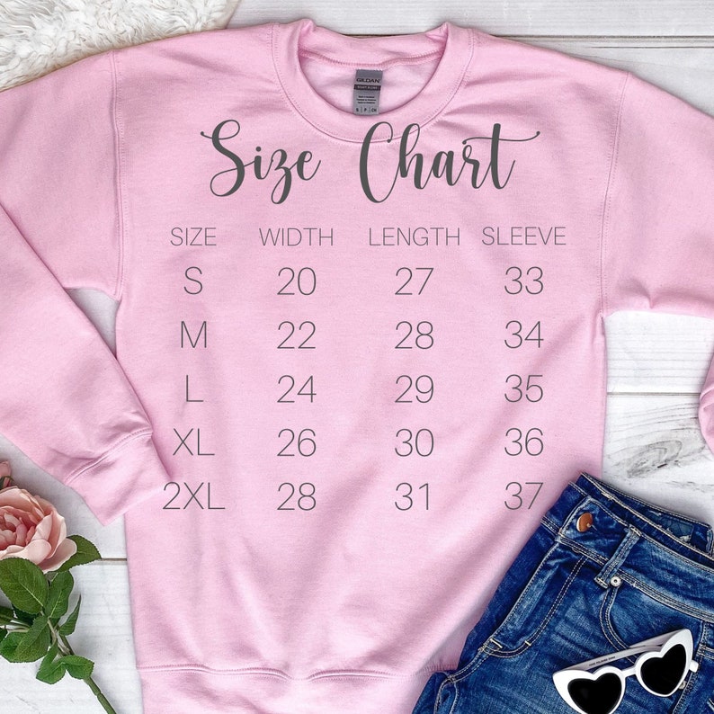 K&ouml;nnte beinhalten: Rosafarbener Pullover mit einer aufgedruckten Gr&ouml;&szlig;entabelle auf der Vorderseite. Die Tabelle listet die Gr&ouml;&szlig;en S, M, L, XL und 2XL mit den entsprechenden Ma&szlig;en f&uuml;r Breite, L&auml;nge und &Auml;rmell&auml;nge in Zoll auf.