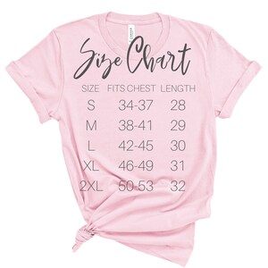 May include: A pink t-shirt with a size chart printed on the front. The chart shows the size, chest measurement, and length in inches.  Size S fits a 34-37 inch chest and is 28 inches long. Size M fits a 38-41 inch chest and is 29 inches long. Size L fits a 42-45 inch chest and is 30 inches long. Size XL fits a 46-49 inch chest and is 31 inches long. Size 2XL fits a 50-53 inch chest and is 32 inches long.