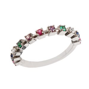 May include: A silver band ring with a row of colorful gemstones. The ring features a variety of colors including red, pink, blue, green, and white.