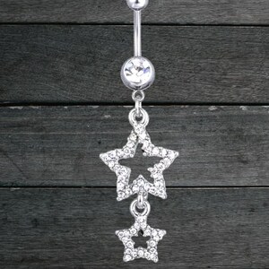 May include: A silver belly button ring with a dangling star design. The top and bottom balls are silver. The dangling stars are encrusted with clear crystals, adding sparkle to the jewelry.