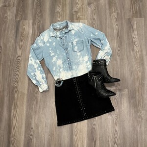 May include: A light blue denim shirt with bleach splatters, a black mini skirt with silver studs, and black ankle boots with silver studs.