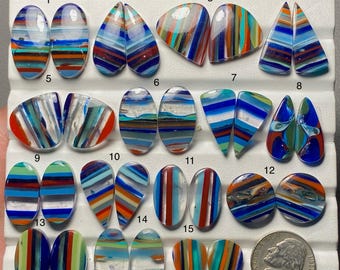 May include: A collection of fifteen pairs of polished, multi-colored glass cabochons arranged in rows on a white display tray, numbered one through fifteen, with a United States nickel coin included for scale next to the final pair.