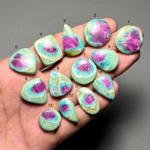 May include: A collection of ruby zoisite gemstones in various shapes, including oval, teardrop, and round. The stones feature a vibrant pink ruby center surrounded by a green zoisite matrix. The gemstones are polished and ready for jewelry making.