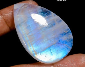 May include: A pear-shaped, polished moonstone gemstone with a milky white base and iridescent blue and white flashes. The gemstone is held in a hand, with the number "2245" in the upper right corner.