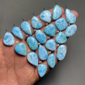 May include: Twenty blue and white cabochon gemstones, each with a unique pattern, are arranged in a hand. The gemstones are numbered 1 through 20.