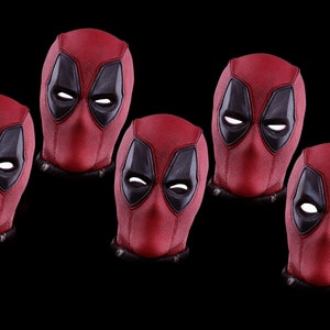 May include: Five red and black Deadpool masks with white eyes. The masks are arranged in a row, with the middle mask slightly higher than the others.