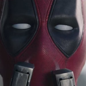 May include: A close-up of a red and black superhero mask with white eyes. The mask has a textured surface and is made of a durable material.