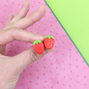May include: A pair of red and green strawberry-shaped earrings. The earrings are made of polymer clay and are about 1 inch in diameter.