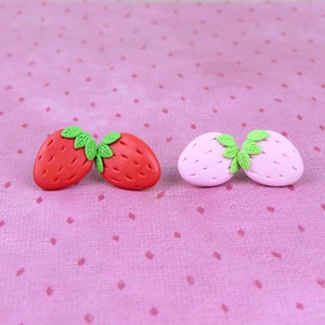 May include: Two pairs of polymer clay earrings shaped like strawberries. One pair is red and the other is pink.