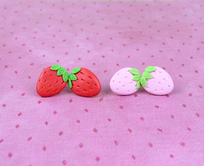 May include: Two pairs of polymer clay earrings shaped like strawberries. One pair is red and the other is pink.