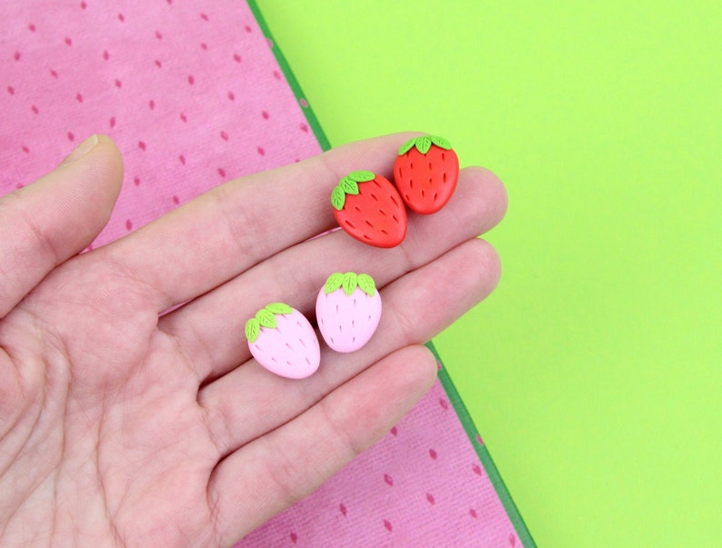 May include: A pair of red and pink strawberry-shaped earrings. The earrings are made of polymer clay and have green leaves.
