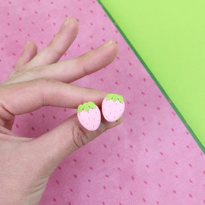 May include: A pair of pink and green strawberry-shaped stud earrings.