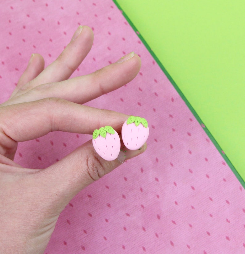 May include: A pair of pink and green strawberry-shaped stud earrings.