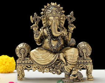 May include: A gold-colored metal statue of Ganesha, the Hindu god of beginnings, sitting on a throne with a mouse at his feet. The statue is intricately detailed and has a traditional design.