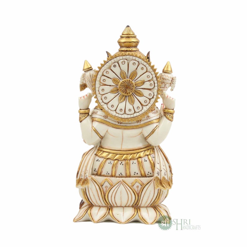 May include: White and gold Ganesha statue with a floral design on the back. The statue is sitting on a lotus base.