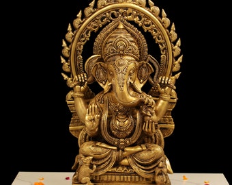 May include: A gold-colored brass statue of Ganesha, the Hindu god of wisdom and prosperity, sitting on a throne with a halo behind him. The statue is intricately detailed with carvings and embellishments.