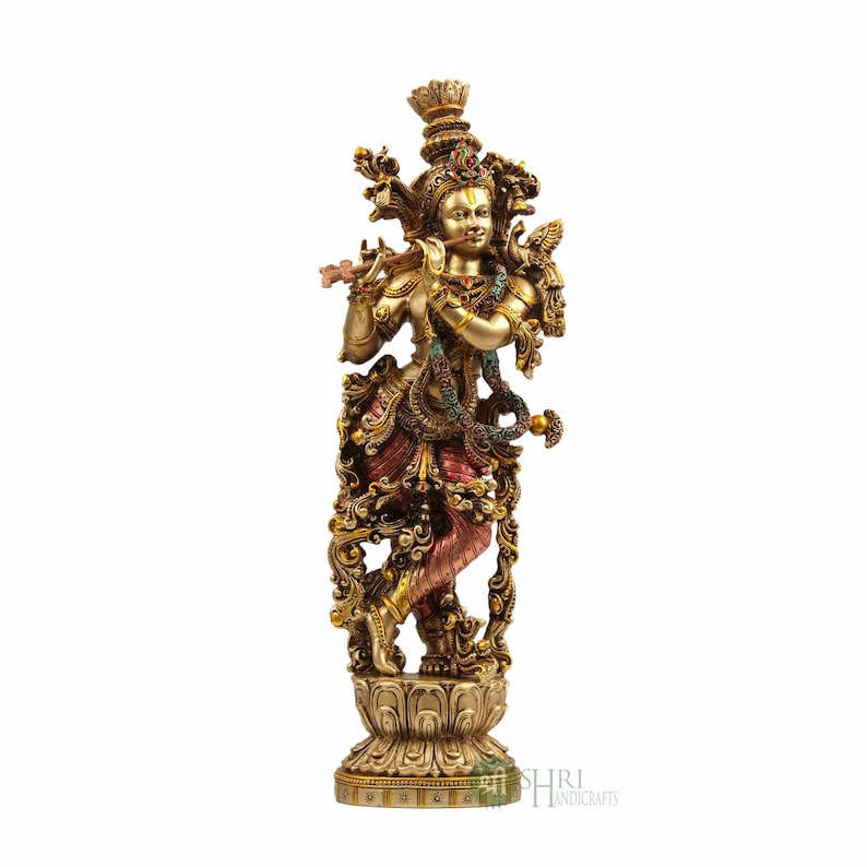 May include: A gold-toned statue of Krishna playing a flute, standing on a decorative base. The statue is intricately detailed with colorful accents and floral patterns.