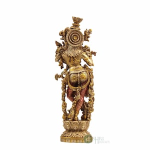 May include: A gold-toned metal statue of a Hindu deity playing a flute. The statue is intricately detailed and features a colorful base.