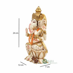 May include: White and gold Ganesha statue sitting on a lotus base with a mouse at its feet. The statue is 24 cm tall, 12 cm wide, and 7 cm deep.