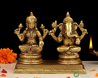 May include: A gold-colored brass statue set of Lakshmi and Ganesha, Hindu deities, sitting on a decorative base. The statues are intricately detailed and have a traditional Indian style.