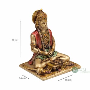 Może przedstawiać: Złota statua hinduskiego boga Hanuman, siedzącego w medytacyjnej pozie na platformie. Statua ma 20 cm wysokości, 16 cm szerokości i 14 cm głębokości. Statua jest ozdobiona kolorowymi klejnotami i misternymi detalami.
