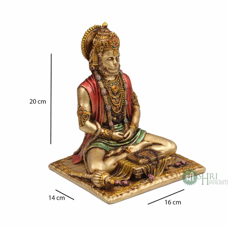 Może przedstawiać: Złota statua hinduskiego boga Hanuman, siedzącego w medytacyjnej pozie na platformie. Statua ma 20 cm wysokości, 16 cm szerokości i 14 cm głębokości. Statua jest ozdobiona kolorowymi klejnotami i misternymi detalami.