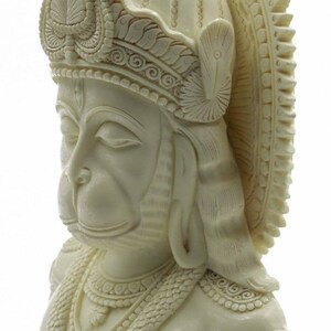 May include: White, detailed, sculpted bust of the Hindu deity Hanuman. The bust is carved with intricate details, including a crown, jewelry, and facial features.