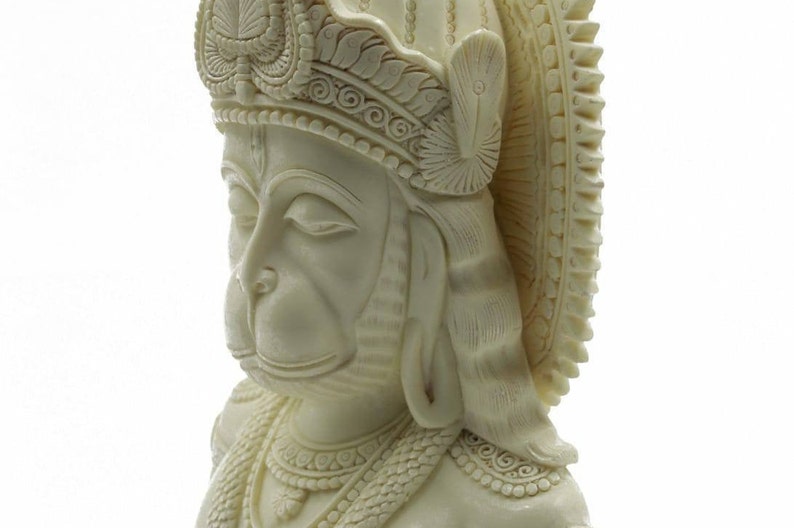 May include: White, detailed, sculpted bust of the Hindu deity Hanuman. The bust is carved with intricate details, including a crown, jewelry, and facial features.