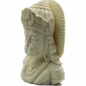 May include: A white, detailed bust sculpture of the Hindu deity Hanuman. The sculpture depicts Hanuman with a crown and a necklace, and his eyes are closed.