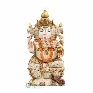May include: White and gold Ganesha statue sitting on a lotus base with a mouse at its feet. The statue is intricately carved with details and has a red and orange garland around its neck.