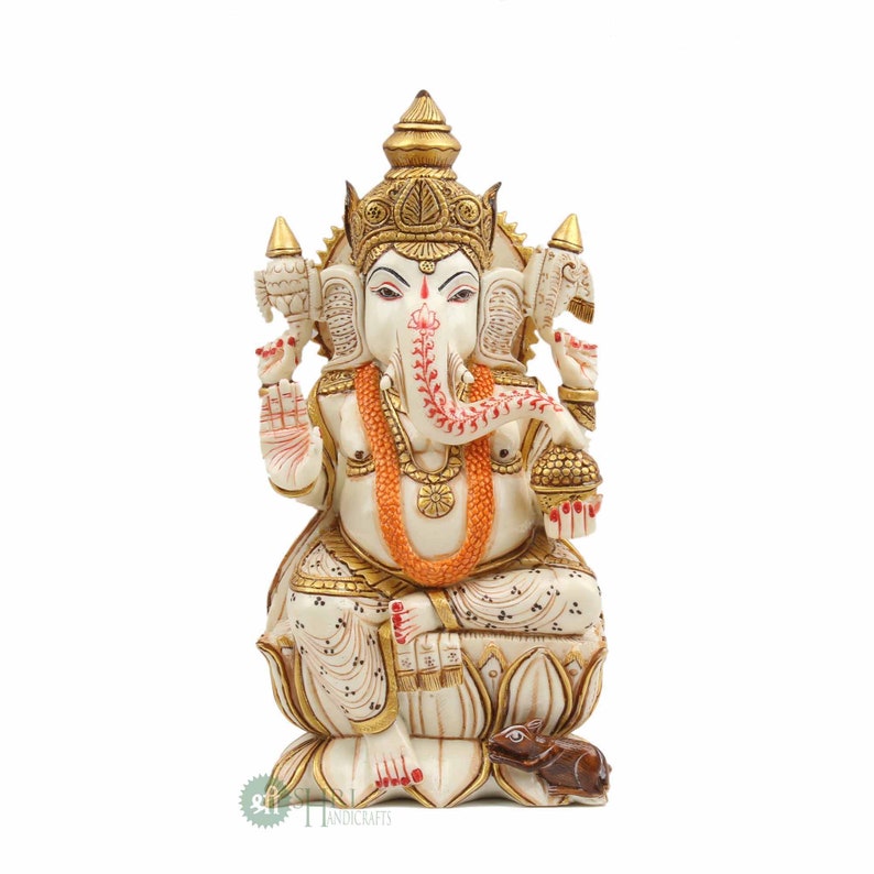 May include: White and gold Ganesha statue sitting on a lotus base with a mouse at its feet. The statue is intricately carved with details and has a red and orange garland around its neck.