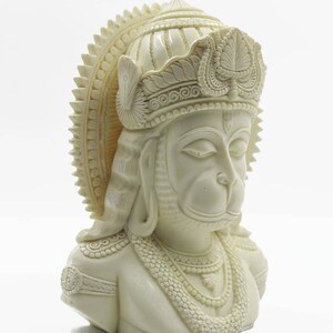 May include: White, detailed bust sculpture of the Hindu deity Hanuman, wearing a crown and ornate jewelry.