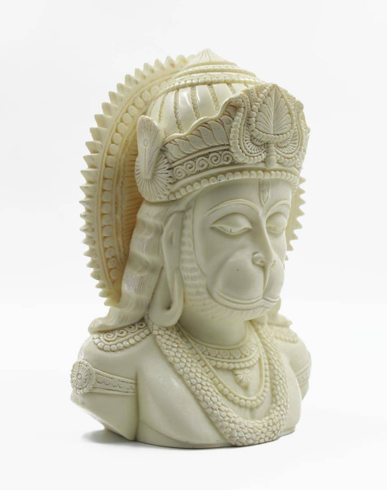 May include: White, detailed bust sculpture of the Hindu deity Hanuman, wearing a crown and ornate jewelry.