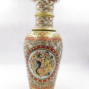 Puede incluir: Un jarrón de mármol blanco con detalles dorados y rojos. El jarrón está decorado con un diseño de pavo real y tiene una base redonda. El jarrón mide aproximadamente 30 cm de alto.