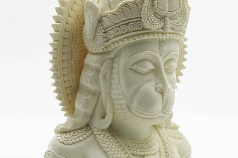 May include: White sculpted bust of the Hindu deity Hanuman, with a detailed crown and closed eyes. The bust is made of a smooth, white material and is a traditional religious art piece.