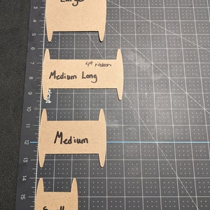 Puede incluir: Cuatro plantillas de carrete de cart&oacute;n para hacer carretes de cinta de diferentes tama&ntilde;os. Las plantillas est&aacute;n etiquetadas como "Large", "Medium Long", "Medium" y "Small".