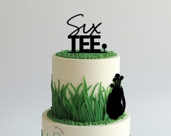 May include: A two-tier cake decorated with green fondant grass and a black acrylic cake topper featuring the text Six TEE and a golf bag silhouette. The topper is placed on the top tier, which is covered in green grass-like texture.