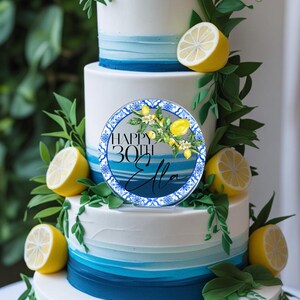 May include: A multi-tiered cake decorated with white, blue, and green accents. The cake is adorned with lemons, greenery, and a circular topper that reads "Happy 30th Ella."