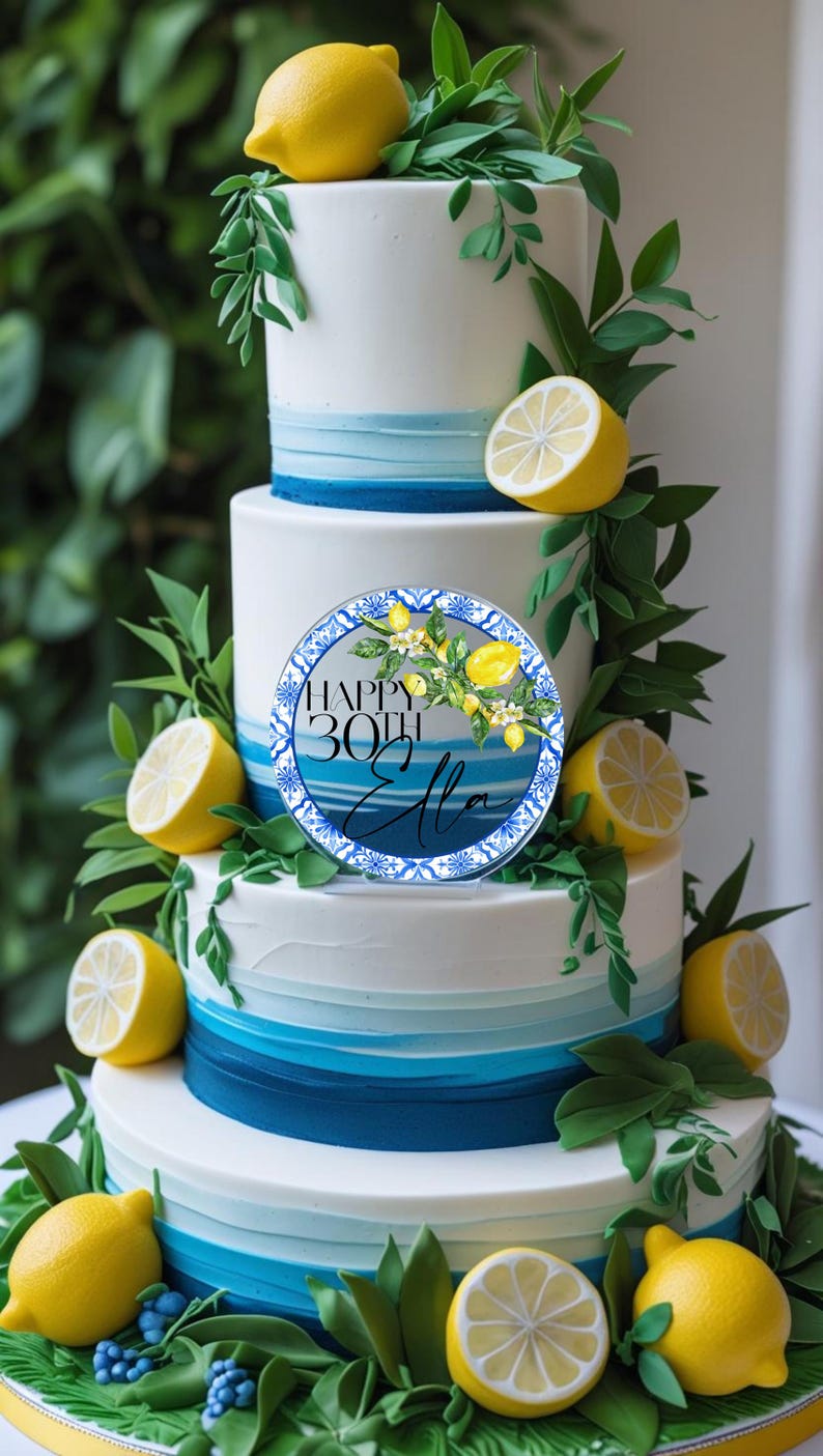 May include: A multi-tiered cake decorated with white, blue, and green accents. The cake is adorned with lemons, greenery, and a circular topper that reads "Happy 30th Ella."