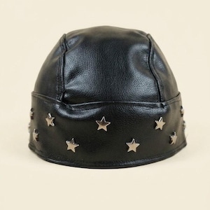 May include: A black faux leather skull cap featuring a textured surface and a wide band around the base. The band is decorated with multiple small, silver-toned metal star-shaped studs evenly spaced around the entire circumference of the hat.
