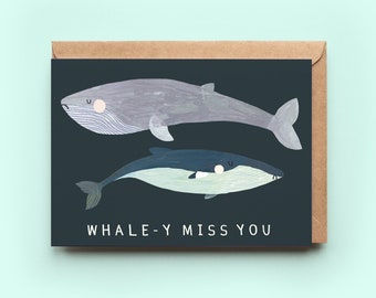 Puede incluir: Una tarjeta de felicitación con un fondo azul oscuro que presenta dos ballenas. La ballena más grande es gris y la más pequeña es azul. El texto "WHALE-Y MISS YOU" está impreso en blanco en la parte inferior de la tarjeta.