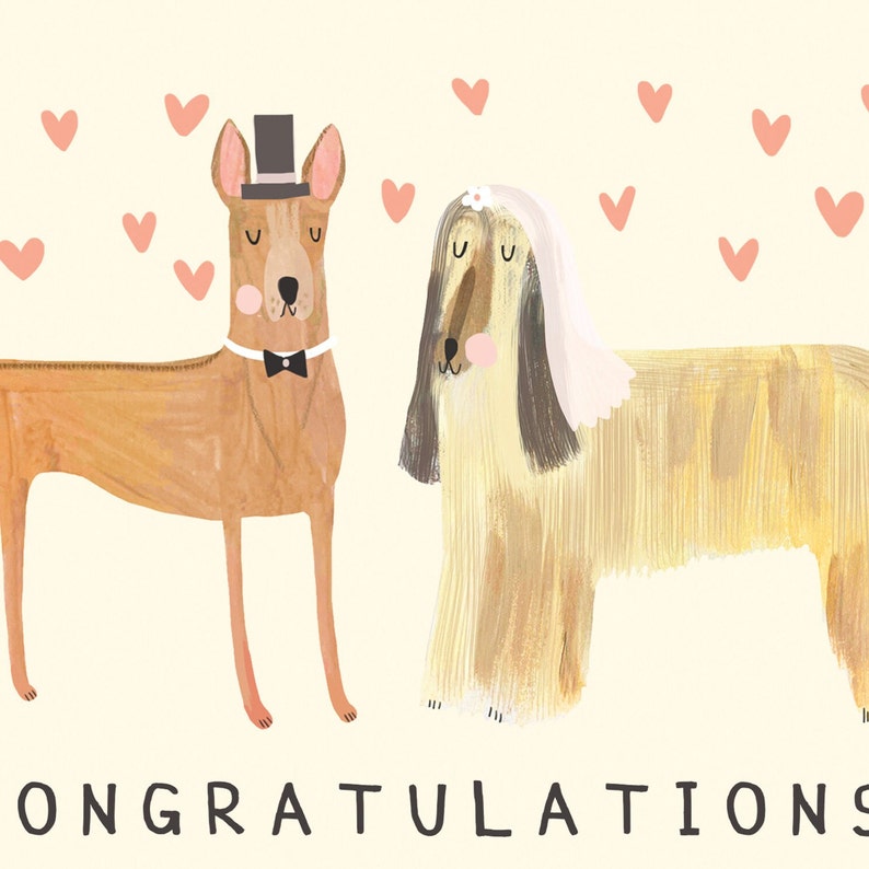 May include: A wedding card featuring a cartoon illustration of two dogs dressed in wedding attire. The dog on the left is wearing a top hat and bow tie, while the dog on the right is wearing a veil. The card has a light yellow background with pink hearts scattered around the dogs. The text "CONGRATULATIONS" is printed in black at the bottom of the card.