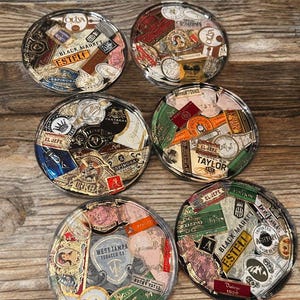Puede incluir: Seis posavasos redondos con tapas de resina transparente, que muestran un collage de etiquetas de cigarros antiguos. Las etiquetas presentan varios colores, fuentes y dise&ntilde;os, incluyendo textos como "OLIVA", "BLACK MARKET" y "ESTELI". Los posavasos est&aacute;n colocados sobre una superficie de madera.