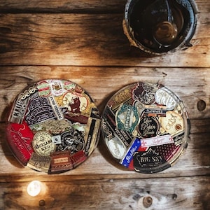 Puede incluir: Dos ceniceros redondos para cigarros llenos de coloridas etiquetas de cigarros, colocados sobre una superficie de madera r&uacute;stica. Las etiquetas presentan varias marcas y dise&ntilde;os, con una est&eacute;tica oscura y envejecida. Un cenicero parcialmente visible est&aacute; en la parte superior.