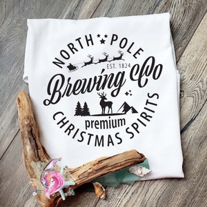 May include: White t-shirt with a black circle design that says "North Pole Brewing Co. Est. 1824 Premium Christmas Spirits". The design includes a reindeer, a Christmas tree, and a sleigh with Santa's reindeer.