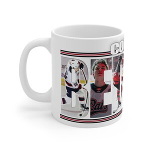 以下が含まれることがあります： 白磁のコーヒーカップ。ホッケー選手のフォトコラージュで「COREY」の文字が作られています。赤、白、黒のカラーで、選手はホッケーのユニフォームを着ており、氷の上でプレーしています。