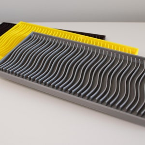 May include: Three dish drying racks, one grey, one yellow, and one black. The racks have a wavy design and are made of a durable plastic.