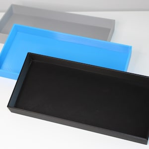 May include: Three rectangular trays stacked on top of each other. The top tray is grey, the middle tray is blue, and the bottom tray is black.