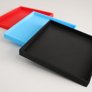 Peut inclure: Trois plateaux carrés, un noir, un bleu et un rouge, empilés les uns sur les autres.